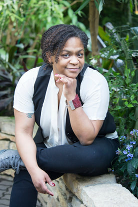 Picture of Illana C. Jordan. Black woman sitting on concrete, with head on arm looking towards camera